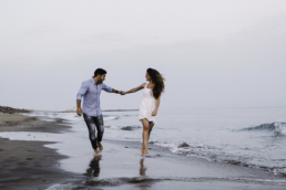 couple holding hands and running in the beach while wind is blowing